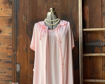 May include: A pink satin nightgown and robe set with a lace trim and pearl necklace. The set is displayed on a mannequin against a wooden background.