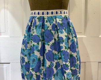 May include: A white apron with a blue floral print and a white lace trim. The apron has a blue and white ribbon waistband.