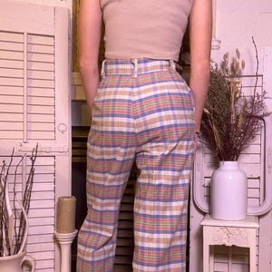 May include: A person wearing a beige ribbed crop top and plaid pants. The high-waisted pants feature a colorful plaid pattern in shades of blue, orange, and green. The pants have a wide-leg design.