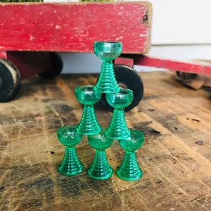 May include: A stack of seven green glass cups with a fluted design. The cups are stacked in a pyramid shape.