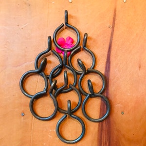 May include: A set of eight black metal curtain rings arranged in a pyramid shape with a pink flower in the center.