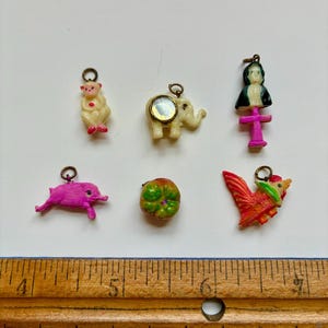 May include: A collection of small, colorful charms, including a monkey, elephant, pig, pumpkin, rooster, and a figure with a cross. The charms are made of plastic and have metal loops for attaching to jewelry or other crafts.