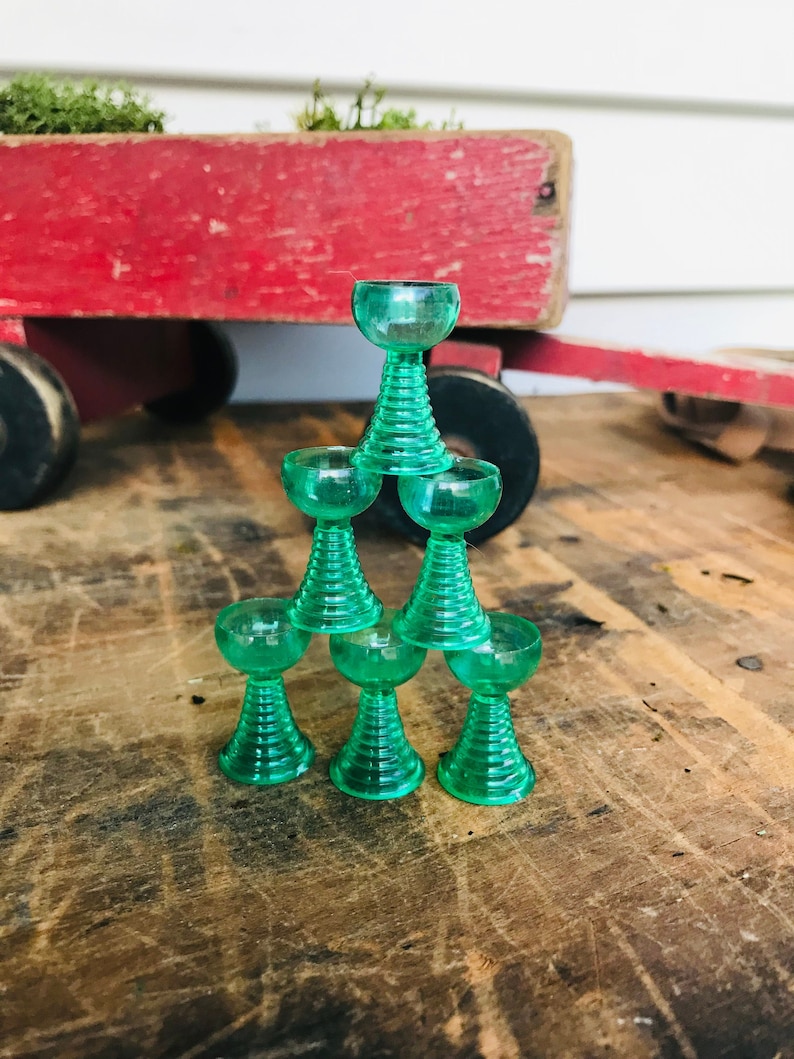 May include: A stack of seven green glass cups with a fluted design. The cups are stacked in a pyramid shape.
