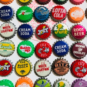 May include: A collection of vintage soda bottle caps featuring various brands and designs. The caps are arranged in a grid pattern and include brands like Crush, 7 Up, Sun Crest, Lotta Cola, Root Beer, and more.
