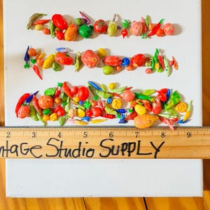 May include: A white canvas with three rows of colorful, sculpted vegetables. The vegetables include tomatoes, peppers, and beans. A wooden ruler with the text "Vintage Studio Supply" is placed across the bottom of the canvas.