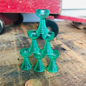 May include: A stack of six green glass cups with a rounded base and a flared top. The cups are stacked in a pyramid shape.