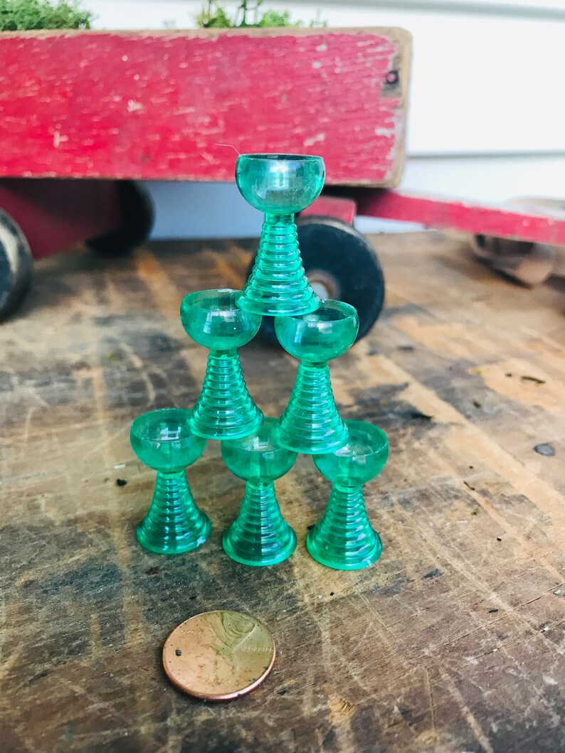 May include: A stack of six green glass cups with a rounded base and a flared top. The cups are stacked in a pyramid shape.
