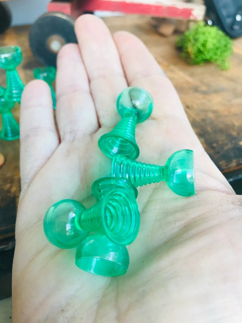 May include: A set of five green plastic toy cups with a ball on top of each cup. The cups are stacked on top of each other.