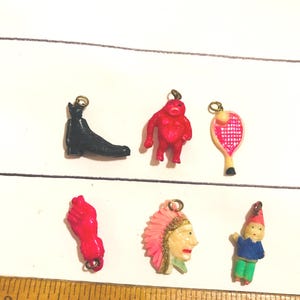 May include: A collection of small, colorful charms. The charms include a black boot, a red ape-like figure, a pink tennis racket, a red fist, a Native American profile, and a gnome. Each charm has a gold-colored loop.