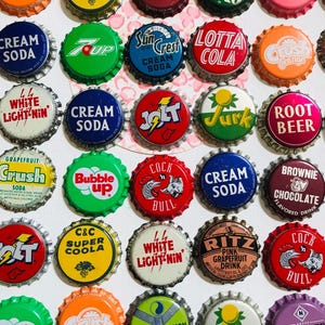 May include: A collection of vintage soda bottle caps, featuring various brands and flavors. The caps display a range of colors, including orange, green, red, and blue, with text such as "Crush Orange," "7 Up," and "Dr. Pepper."