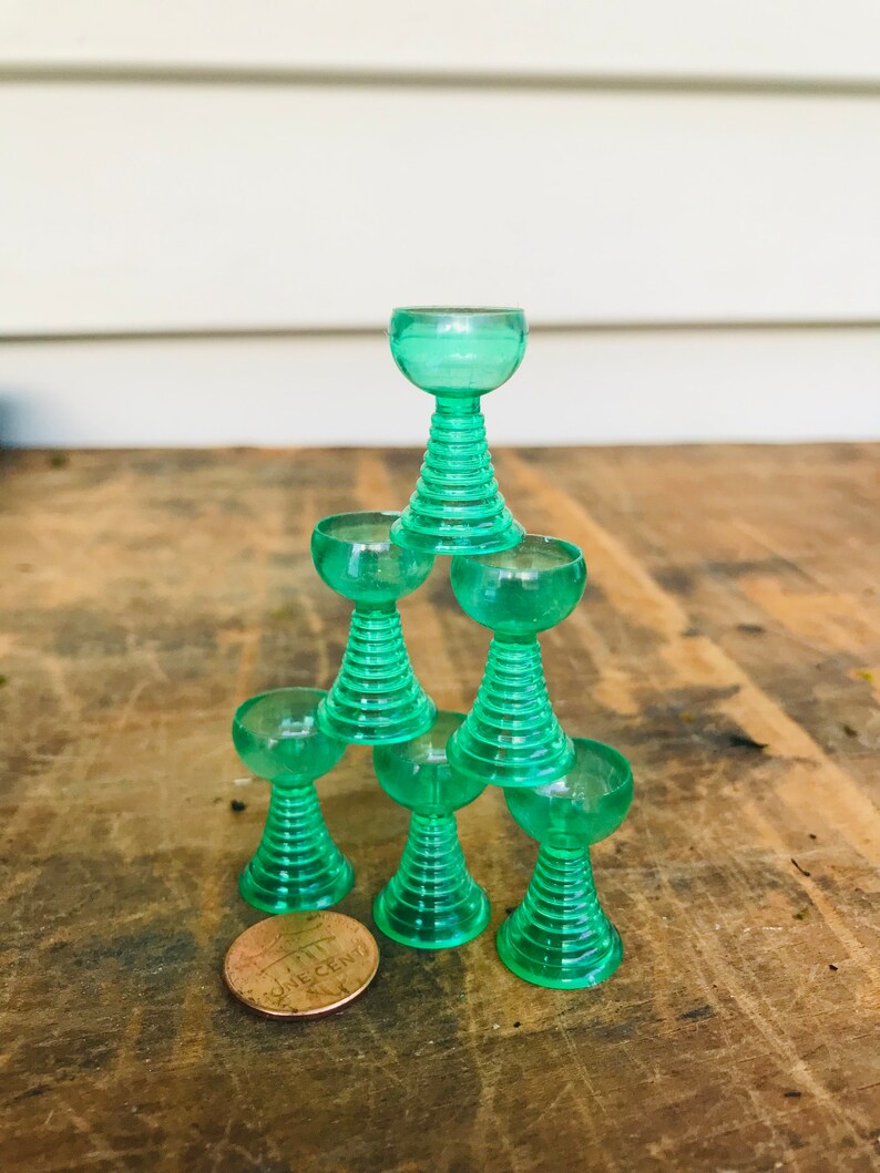 May include: A stack of six green glass goblets with a fluted design. The goblets are stacked in a pyramid shape, with the smallest goblet on top. A penny is in the foreground.