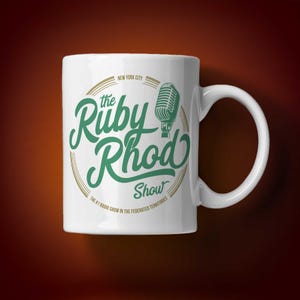 May include: White ceramic mug with the words "the Ruby Rhod Show" in green script, and a vintage microphone graphic. The mug also includes the text "New York City" and "The #1 Radio Show in the Federated Territories."