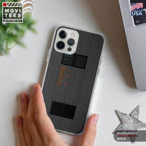 May include: A clear phone case with a gray and black design featuring the text "TARS" and a grid pattern. The case is for an iPhone 14 Pro Max.