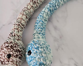 Peut inclure: Deux jouets serpent en peluche faits à la main. L'un est marron et blanc, l'autre bleu et blanc. Chacun a un bouton noir pour les yeux. Les serpents sont faits d'un fil doux et texturé.