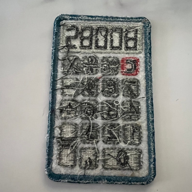 May include: A blue and white embroidered patch of a calculator with the number "28008" displayed on the screen.