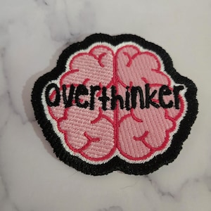 Pode incluir: Patch bordado com um design de cérebro rosa e a palavra "Overthinker" em branco. O gráfico do cérebro tem um contorno vermelho e uma borda preta. Este patch é adequado para jaquetas, bolsas ou outros itens de tecido.