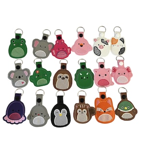 Puede incluir: Una colección de llaveros bordados con forma de animales de varios colores. Los llaveros incluyen una rana, un elefante, un cerdo, una vaca, un gato, un koala, un dinosaurio, un perezoso, un cerdo, un ajolote, un pato, un pingüino, un zorro y un castor.