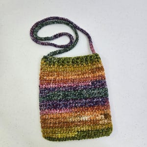 May include: A handmade crochet crossbody bag in a spectrum of colors, including green, orange, purple, and brown. The bag features a textured stitch pattern and a matching strap, perfect for carrying essentials.
