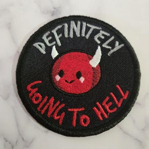 May include: Embroidered patch with the text "DEFINITELY GOING TO HELL". The patch is round, with a black background and red lettering. A red devil face with white horns is in the center.