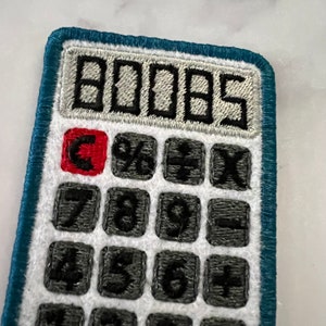 May include: A blue and white embroidered calculator patch with a red C button and the number 0005 displayed on the screen.