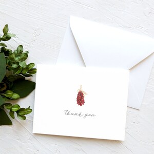 May include: A white thank you card with a red and gold illustration of a pine cone. The text "thank you" is written in cursive on the card.