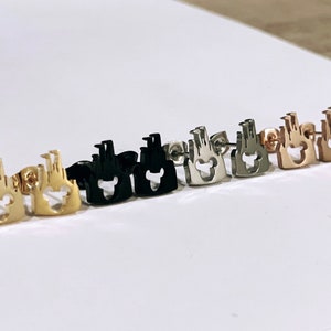 May include: A set of six pairs of earrings featuring a castle silhouette with a Mickey Mouse head cutout. The earrings are available in gold, rose gold, silver, and black.
