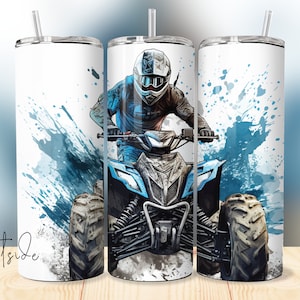 Puede incluir: Un vaso blanco con un diseño de un piloto de quad, con salpicaduras de pintura azules y grises. El vaso tiene una tapa plateada y una pajita. También es visible el texto "Westside Vinyl".