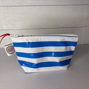 May include: A white and blue striped cosmetic bag with a zipper closure. The bag has a red ribbon attached to the zipper pull. A small tag with the letters "KT" is attached to the bag.
