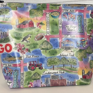 May include: A white zippered pouch with a colorful map design of Fargo, North Dakota. The map features landmarks like Island Park, Lindenwood Park, and the Fargo Theatre. The pouch has a red and white "GO" logo on the front.