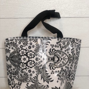 May include: A black and white tote bag with a floral pattern. The bag has black handles and a white background with black floral designs.