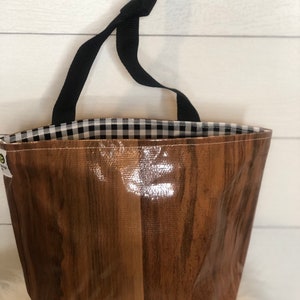 May include: A tote bag with a glossy, wood-grain exterior and a black and white gingham interior. The bag has a black strap and is designed to be carried by hand. The bag is made of a durable material.