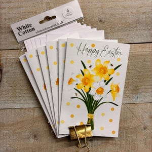 May include: A pack of six Easter cards with envelopes. Each card displays a watercolour bouquet of yellow and white daffodils, the words "Happy Easter", and yellow polka dots. The cards are held together with a gold clip.