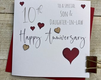 May include: A white card with the text "10th Happy Anniversary" in gray script. The card also has the text "To a special Son & Daughter-in-Law" in gray. There are several small red and brown hearts on the card.