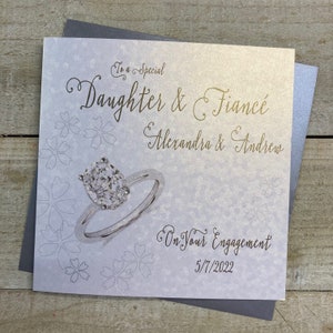K&ouml;nnte beinhalten: Eine wei&szlig;e Karte mit einem goldenen Glitzerdesign, das einen Diamantring und den Text "To a Special Daughter & Fianc&eacute; Alexandra & Andrew On Your Engagement 5/7/2022" zeigt.