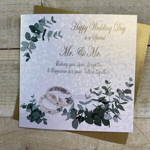 K&ouml;nnte beinhalten: Eine Hochzeitskarte mit wei&szlig;em Hintergrund und goldener Schrift. Die Karte zeigt ein Paar silberne Ringe mit den Worten "I Do" auf einem der Ringe. Die Karte zeigt auch ein Blattdesign in Gr&uuml;n- und Graut&ouml;nen. Der Text auf der Karte lautet: "Happy Wedding Day to a Special Mr. & Mr. Wishing you Love, Laughter & Happiness for your Future together."