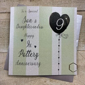 May include: A 9th pottery anniversary greeting card. The card features a striped green and white design with the text "To a Special Son & Daughter-in-law" and "Happy 9th Pottery Anniversary". A black heart-shaped balloon with the number 9 is shown.