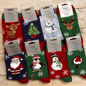 以下が含まれることがあります： トナカイ、クリスマスツリー、シロクマ、サンタクロース、ペンギン、雪だるま、鳥など、さまざまなデザインのクリスマスをテーマにした靴下の詰め合わせ。各ペアには「White Cotton Luxury Socks」と書かれた白いタグが付いています。
