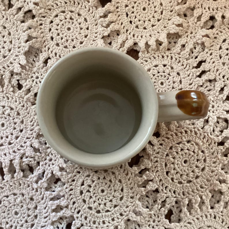 Pu&ograve; includere: Una tazza da caff&egrave; in ceramica color crema con un manico marrone. L'interno della tazza &egrave; di colore verde chiaro. La tazza &egrave; vista dall'alto.