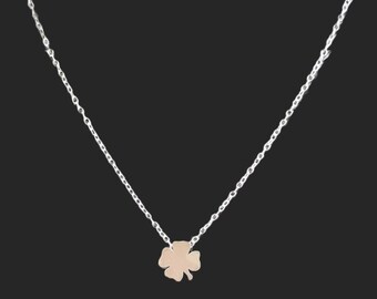 May include: A silver chain necklace with a small, rose gold four-leaf clover pendant.