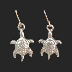 May include: A pair of silver turtle earrings with gold hooks. The turtles have a textured shell and are facing forward.
