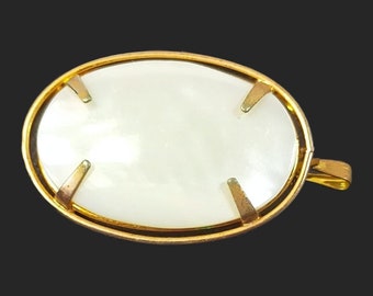May include: A gold-toned oval brooch with a white, pearlescent center. The brooch has a simple, elegant design.