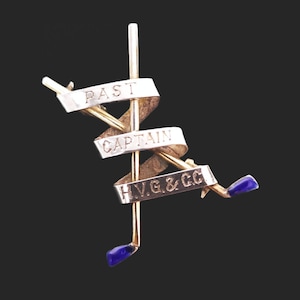 May include: Gold and silver pin with blue enamel accents. The pin features two crossed golf clubs with a ribbon that reads "Past Captain H.V.G. & C.C."