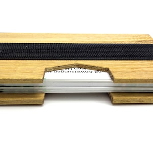 May include: A wooden card holder with a black elastic band. The holder is made of light-colored wood and has a slot to hold cards. The cards are visible in the center of the holder. The holder is designed to be compact and stylish.
