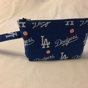 May include: Blue zippered pouch featuring the Los Angeles Dodgers logo and baseballs. The pouch has a small handle and is made of fabric. The design includes the team's initials and the word "Dodgers" in white.