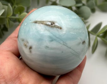 May include: A smooth, light blue and white sphere of polished blue calcite, a crystal known for its calming energy.