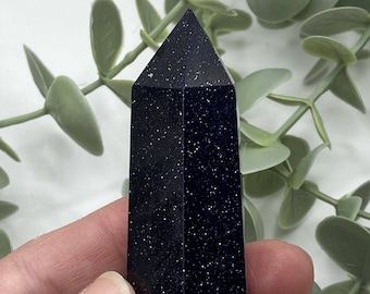 May include: A dark blue, star-shaped, polished crystal point. The crystal has a sparkly, glittery appearance.