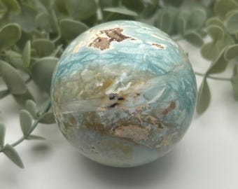 May include: A blue and brown sphere with a swirling pattern. The sphere is made of a natural material, possibly a type of agate or jasper. It is a decorative object that could be used for meditation or as a paperweight.