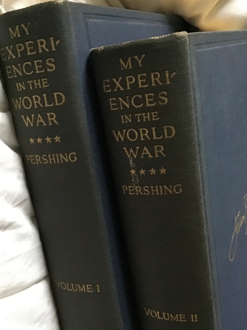 May include: Two dark blue hardcover books with gold lettering. The books are titled "My Experiences in the World War" by Pershing. The first book is labeled "Volume I" and the second book is labeled "Volume II".