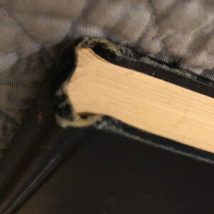 May include: Close-up of the top edge of a black hardback book with a worn, slightly frayed spine. The pages are a creamy white colour.