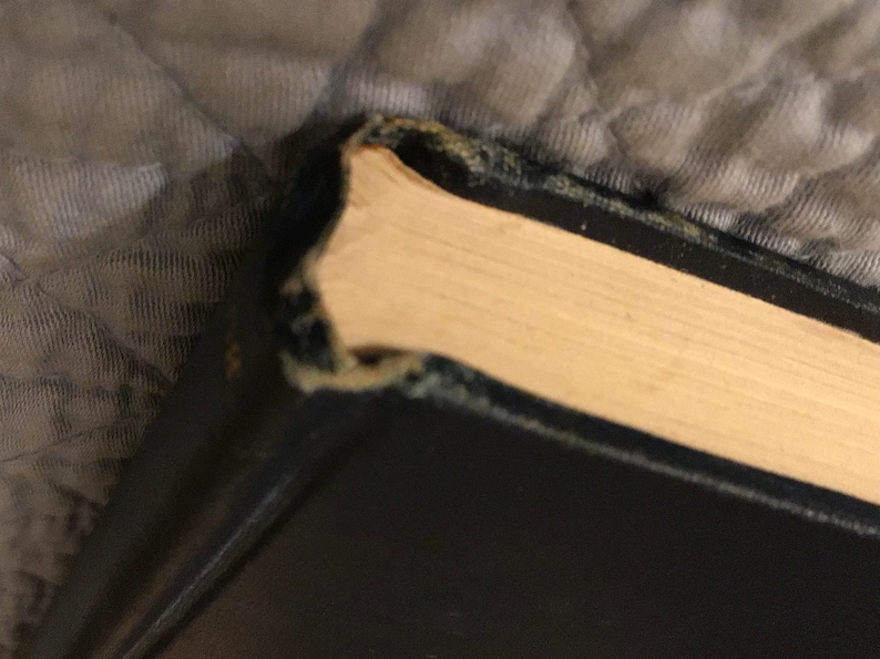 May include: Close-up of the top edge of a black hardback book with a worn, slightly frayed spine. The pages are a creamy white colour.